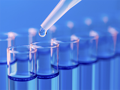 Close-up shot of the tops of long vials full of liquid. An eyedropper is dripping the liquid into one of the vials.